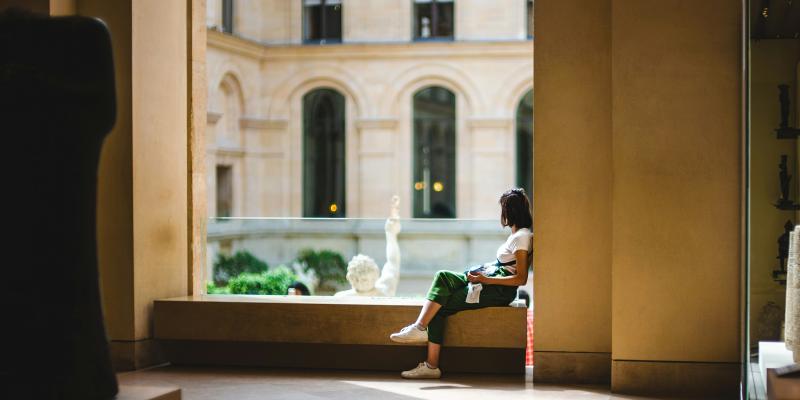 Henkilö istuu ikkunan syvennyksessä ajatuksiinsa uppoutuneena.
