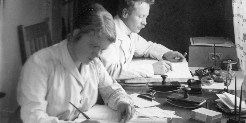 Mustavalkoinen kuva vuodelta 1918, nainen ja mies tekevät muistiinpanoja kirjoituspöydän äärellä. Mies on kauppias Otto Selenius Oravaiselta, nainen tunnistamaton.