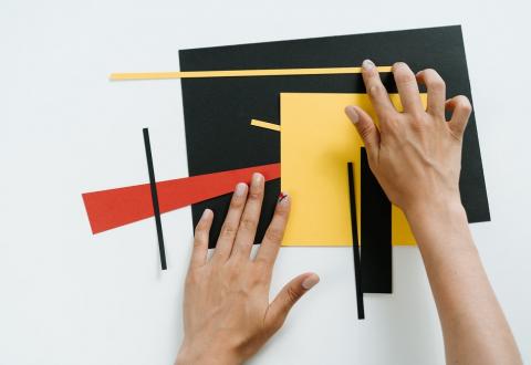Kuvituskuva, jossa käsipari sommittelee värikkäitä paperin paloja.